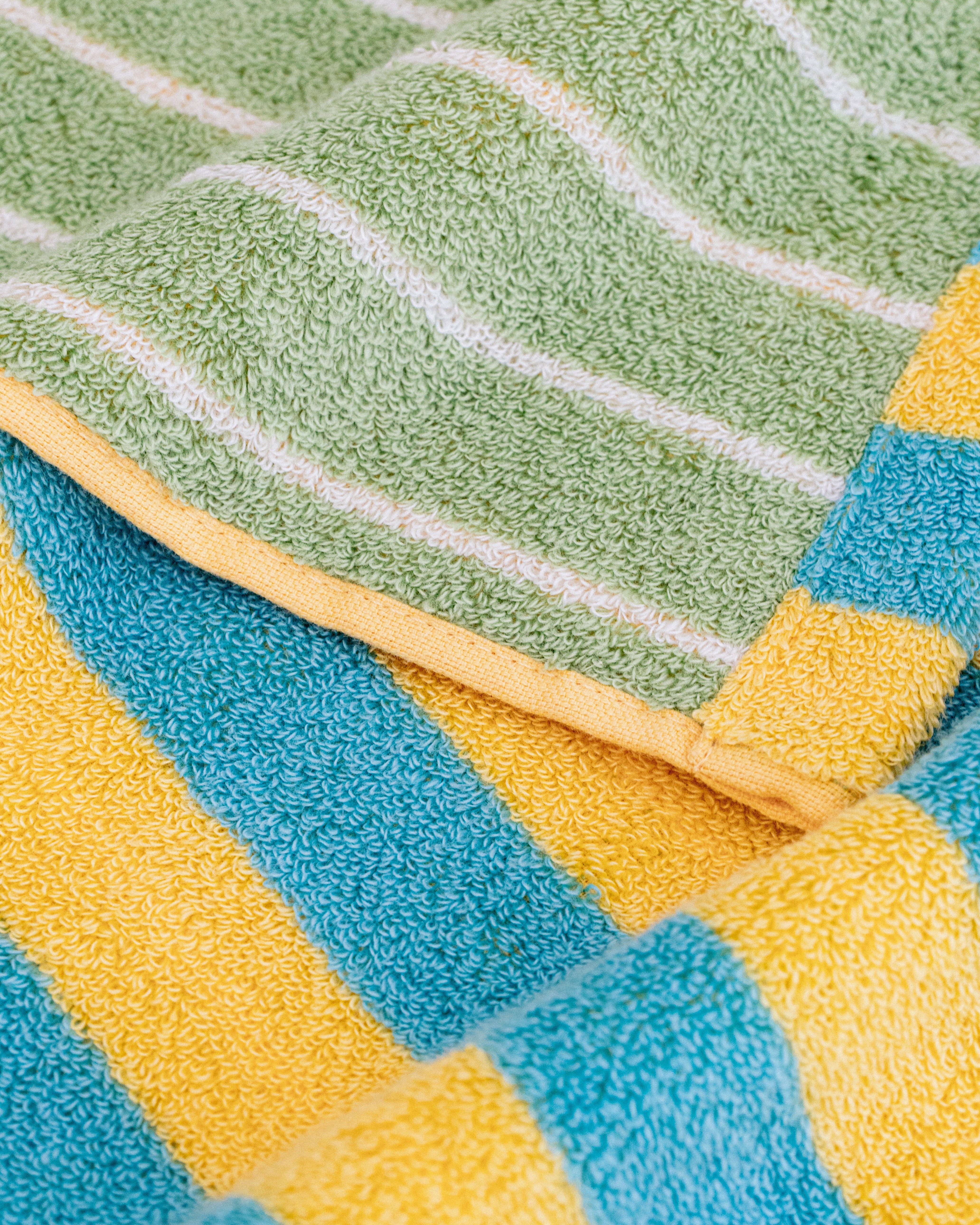 Close-up of yellow and turquoise striped towel fabric beside pale green fabric with fine light stripes and yellow edging.